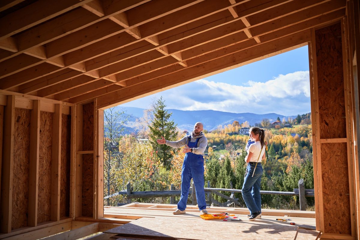 Father, mother and son building wooden frame house. Male designer in blue overalls showing future home, standing on terrace on construction site. Carpentry, family concept.